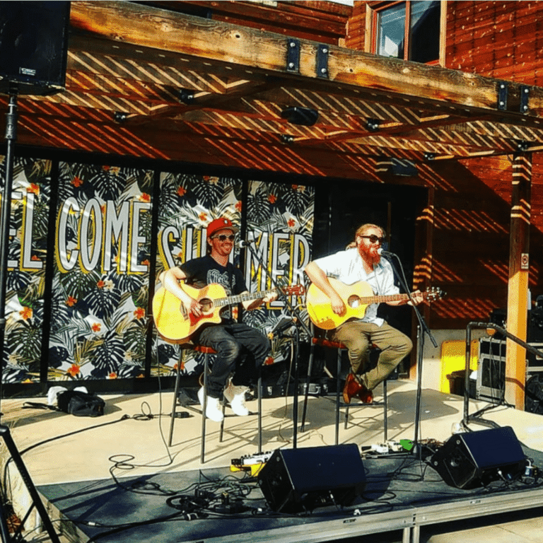 Three musicians playing acoustic guitars on an outdoor stage.